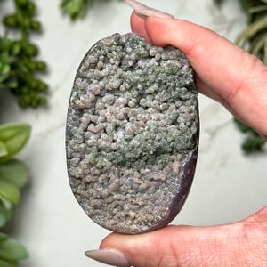 May include: A close-up of a purple and green agate stone with a unique, textured surface. The stone is covered in small, round bumps and has a smooth, polished finish.