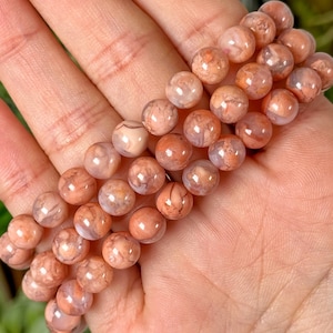 Puede incluir: Un conjunto de pulseras hechas con cuentas de ágata rosa y blanca. Las cuentas tienen un patrón de mármol y son redondas.