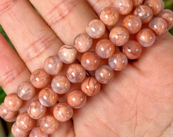 Op de afbeelding: Een stapel armbanden gemaakt van roze en witte agaat kralen. De kralen hebben een marmerpatroon en zijn rond.