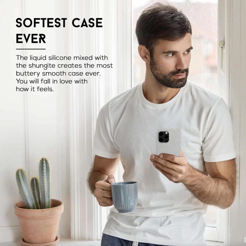 May include: A light gray phone case held by a person wearing a white t-shirt. The case has a square camera module. Text on the image reads "SOFTEST CASE EVER". A blue mug and a potted cactus are also visible.