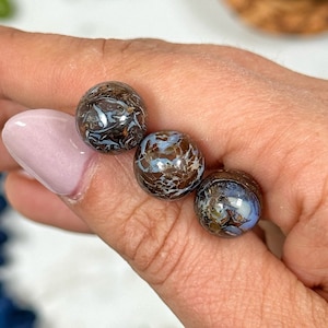 May include: Three round, brown and blue opal beads with a swirling pattern.