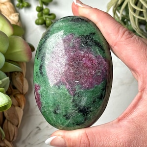 Może przedstawiać: Polerowany zielony i różowy kamień szlachetny o gładkim, owalnym kształcie. Kamień ma marmurkowy wzór w kolorze zielonym, różowym i czarnym.