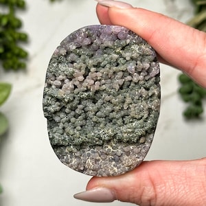 May include: A green and purple agate slice with a unique, textured surface. The agate has a layered appearance with a variety of shades of green and purple.
