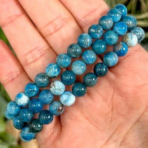 May include: Three blue gemstone bracelets with round beads. The beads are a gradient of blue, from a darker blue to a lighter blue.