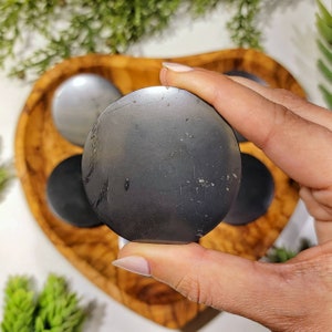 Puede incluir: Una piedra de palma de obsidiana negra con una superficie lisa y pulida. La piedra es redonda y tiene un ligero brillo.