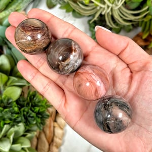 Może przedstawiać: Cztery polerowane kule z kamieni szlachetnych w różnych odcieniach brązu, różu i szarości. Kule są gładkie i mają naturalny, marmurowy wygląd.