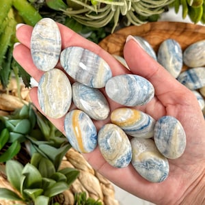 May include: A collection of blue, white, and yellow banded tumbled stones. The stones are smooth and polished, with a variety of patterns and swirls.