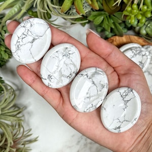 May include: Four white howlite palm stones with gray veining. The stones are smooth and polished, and they are arranged in a hand.