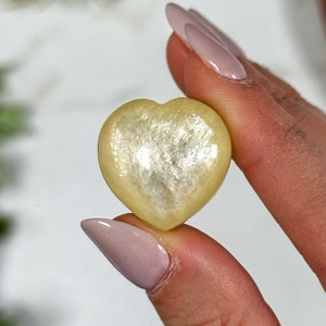 May include: A heart-shaped, pale yellow selenite crystal with a shimmering, iridescent finish.