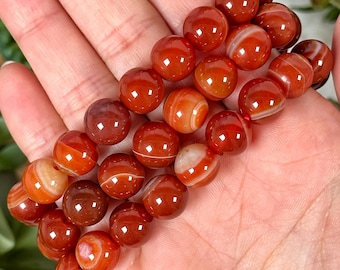 May include: Three stacked bracelets made of red carnelian beads with white stripes. The beads are round and polished.