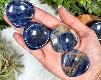 May include: Four heart-shaped polished blue and white Sodalite crystal stones. The stones are smooth and have a natural, striated pattern.