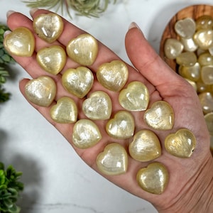 May include: A collection of golden selenite heart shaped crystals. The crystals are smooth and polished, with a translucent, milky white color.