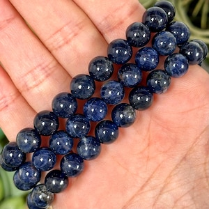 Puede incluir: Una pila de tres pulseras de piedras preciosas azules con cuentas redondas. Las pulseras están hechas de cuentas redondas de color azul oscuro, casi negro.
