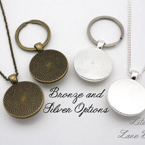 K&ouml;nnte beinhalten: Zwei Halsketten mit einem runden Anh&auml;nger, eine in Bronze und eine in Silber. Die Anh&auml;nger haben ein strukturiertes Design. Die Halsketten befinden sich auf einem wei&szlig;en Hintergrund. Bronze- und Silberoptionen. Literary Lane Boutique.