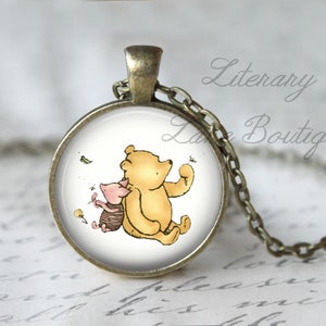 Peut inclure: Un collier Winnie l'ourson et Porcinet avec une cha&icirc;ne en bronze et un pendentif rond en verre repr&eacute;sentant un fond blanc avec une image de dessin anim&eacute; de Winnie l'ourson et Porcinet. Le pendentif est entour&eacute; d'un cadre en bronze.