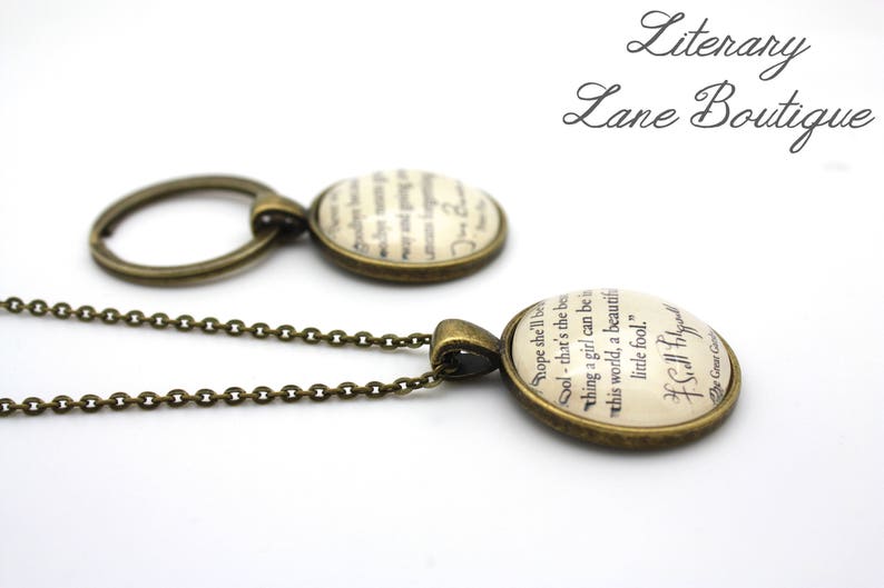 May include: A bronze chain necklace with a bronze key ring charm and a round glass pendant featuring a vintage book page with the text "hope she'll be Sol - that's the be thing a girl can be in this world, a beautiful little fool." - F. Scott Fitzgerald The Great Gatsby"