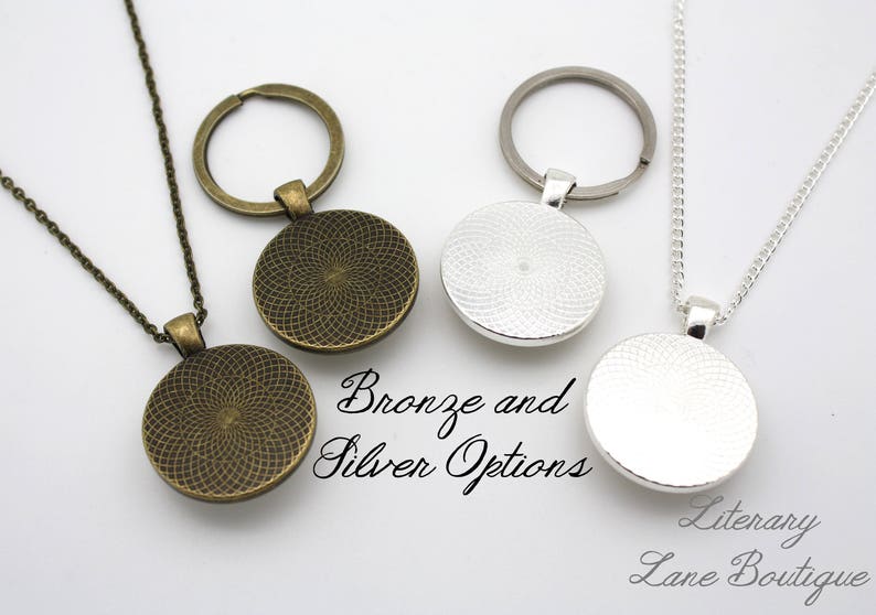 Pode incluir: Dois colares com um pingente circular, um de bronze e outro de prata. Os pingentes t&ecirc;m um design texturizado. Os colares est&atilde;o sobre um fundo branco. Op&ccedil;&otilde;es de bronze e prata. Literary Lane Boutique.