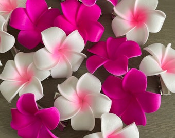 Puede incluir: Una colección de pinzas para el cabello con flores de plumeria de cinco pétalos en magenta vibrante sólido y blanco con puntas magenta. Cada flor está unida a una pinza de cocodrilo de metal plateado visible en la parte inferior.