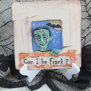 Puede incluir: Una imagen enmarcada en blanco con una cara de monstruo verde asomándose por una ventana con fondo azul y estrellas. El monstruo tiene una cicatriz cosida en la frente y sostiene un cartel que dice "Can I be Frank?"
