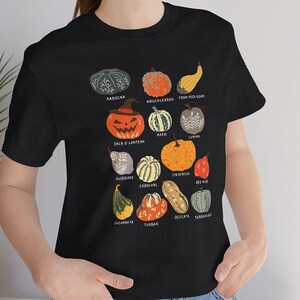 May include: Black t-shirt featuring a colorful illustration of various pumpkins, including Jack O'Lantern, Hubbard, and Cinderella. Each pumpkin is labeled with its name. A fun and educational design for fall or Halloween.