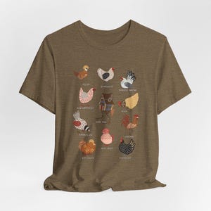 May include: A brown t-shirt featuring a colorful illustration of various chicken breeds, each labeled with its name. The design includes breeds like Polish, Wyandotte, and Japanese Bantam, among others. The artwork is detailed and whimsical, perfect for poultry enthusiasts.