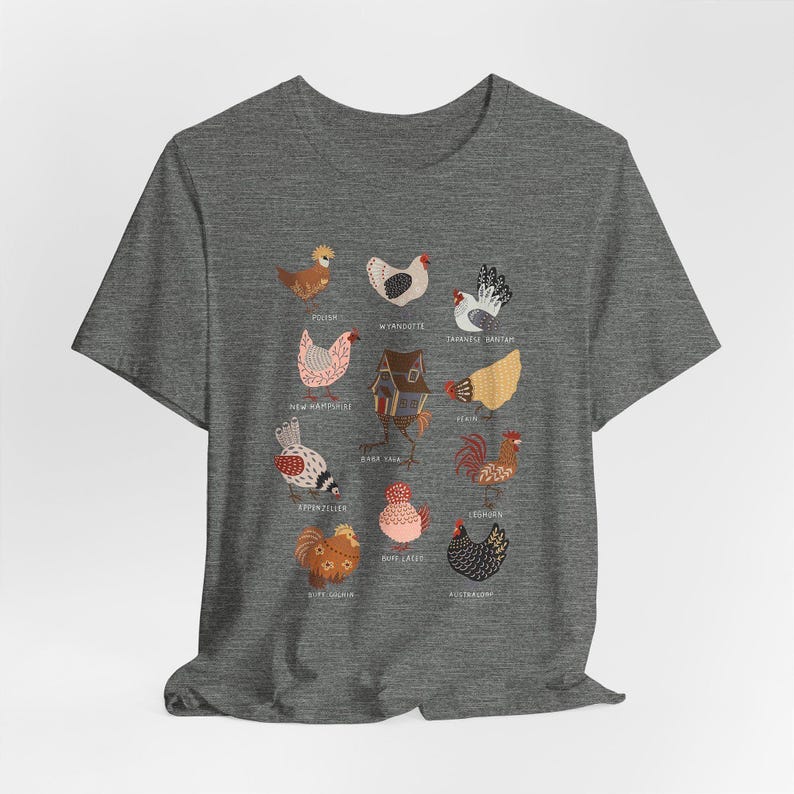 May include: A heather gray t-shirt featuring colorful illustrations of various chicken breeds. The shirt displays detailed drawings of chickens with names like Polish, Wyandotte, and Japanese Bantam. The design is centered on the front of the shirt.