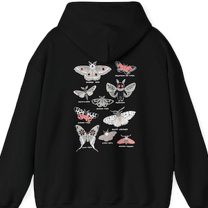 Peut inclure: Sweat à capuche noir avec un motif détaillé de différentes espèces de papillons de nuit. Le motif comprend des illustrations de papillons de nuit avec des noms tels que "Emperor Moth" et "Giant Leopard" en blanc et rose. Le sweat à capuche a une capuche à cordon.