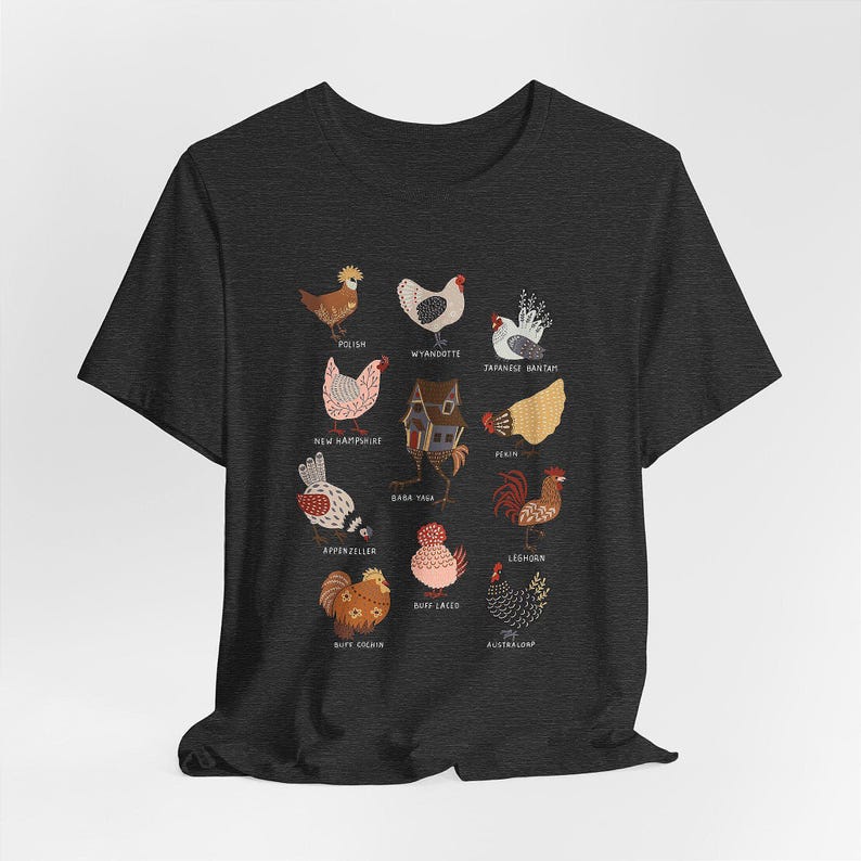 May include: Dark gray t-shirt featuring a colorful illustration of various chicken breeds, including Polish, Wyandotte, and Japanese Bantam. The design includes a small house and text labels identifying each breed. A unique and educational design.