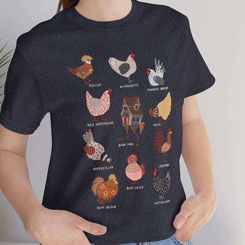 May include: Navy blue t-shirt featuring colorful illustrations of various chicken breeds, including Polish, Wyandotte, and Japanese Bantam. Each chicken is labeled with its breed name. The shirt is a comfortable, casual wear.