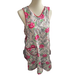 May include: A sleeveless apron with a floral pattern featuring large pink roses, white daisies, and green leaves on a light gray background. The apron has a red trim and a pocket.