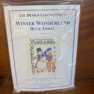 Può includere: Un kit per punto croce intitolato "Winter Wonderland Huck Towel" di The Design Connection. Il kit presenta un pupazzo di neve, un coniglio e le parole "Winter Wonderland" in un disegno a punto croce. Include filo, tessuto, ago e istruzioni.