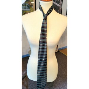 May include: A patterned tie with a dark blue, green, and burgundy color scheme. The tie is made of a silky material and has a geometric pattern.