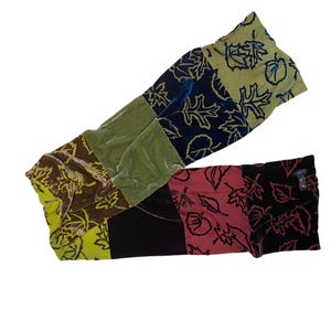 May include: A colorful patchwork scarf made of velvet with a leaf pattern. The scarf is made of six different colors: green, blue, brown, black, red, and yellow.