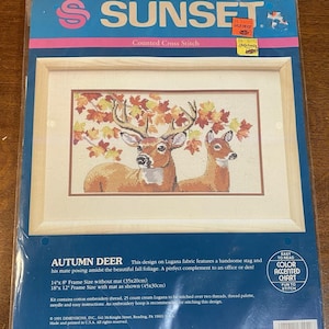 May include: A Sunset counted cross stitch kit featuring an autumn scene with two deer under fall foliage. The kit includes cotton embroidery thread, a color-accented chart, and easy instructions. Frame size without mat is 14" x 8" (35x20cm).