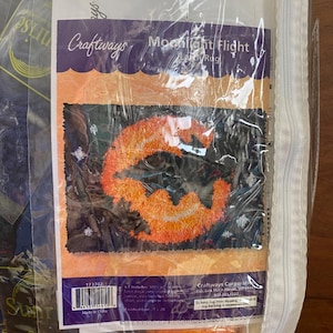 Peut inclure: Un kit de tapis à boucler Craftways, intitulé "Moonlight Flight". Le kit présente un motif de citrouille orange sur fond sombre. L'emballage comprend le logo Craftways et des informations sur le produit.