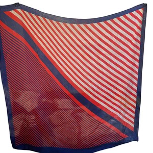 May include: A square scarf with a bold design. The scarf features diagonal stripes in red and white, with a section of red and navy blue diagonal lines. A navy blue border frames the scarf.