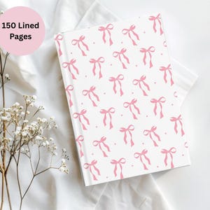 Può includere: Un quaderno bianco con un motivo a fiocco rosa. La copertina presenta un motivo ripetuto di fiocchi rosa su sfondo bianco. Il testo "150 Lined Pages" è in un cerchio rosa. Il quaderno è su una superficie bianca con fiori.