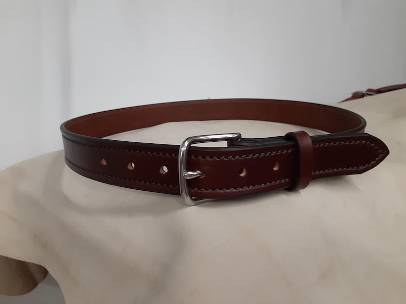 May include: A brown leather belt with a silver-colored buckle. The belt has a classic design with visible stitching and several holes for adjustment. The leather appears to be of high quality.