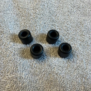 May include: Four small, black rubber feet, each with a cylindrical shape and a central hole. The feet are evenly spaced on a textured, light gray surface. These are likely used as protective bumpers or supports.