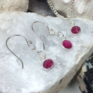 May include: A set of silver earrings and a necklace with pink gemstone pendants. The earrings have a hook fastening and the necklace has a chain style.