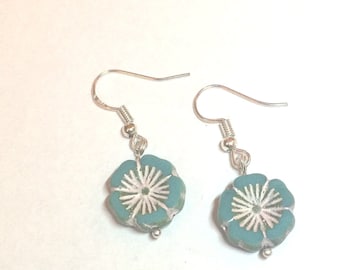 Puede incluir: Un par de pendientes colgantes de plata con cuentas de color azul turquesa en forma de flor. Las cuentas tienen un centro blanco con un diseño de estrella.