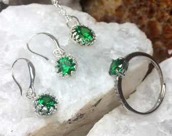 Puede incluir: Un conjunto de joyas de plata con piedras preciosas verdes. El conjunto incluye un collar, un par de pendientes y un anillo.