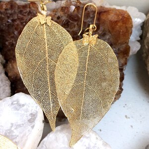 May include: A pair of gold leaf earrings with a delicate butterfly design. The earrings are made from real leaves that have been gilded with gold.