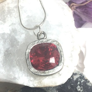 Può includere: Una collana con catena d'argento con un ciondolo quadrato con una grande pietra preziosa rossa sfaccettata.