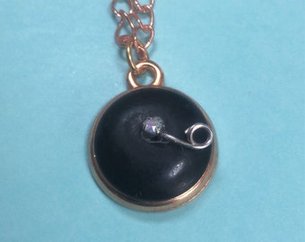 May include: A gold chain necklace with a black circular pendant. The pendant has a gold rim and a small silver detail.