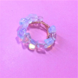 May include: A ring made with iridescent white opal stones wrapped in copper wire.