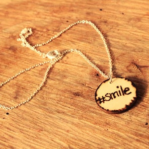 May include: A silver chain necklace with a wooden pendant that says "#smile" on it.