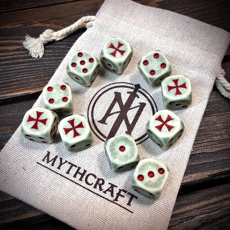 May include: A set of ten dice with red markings and crosses, resting on a beige drawstring bag. The dice are light green with red pips and crosses. The bag has the text "MYTHCRAFT" printed on it.