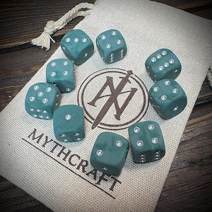 May include: Nine teal dice with silver pips are arranged on a beige cloth bag. The bag features the text "MYTHCRAFT" and a logo with a sword and the letter "N". The dice are displayed in a circular pattern.