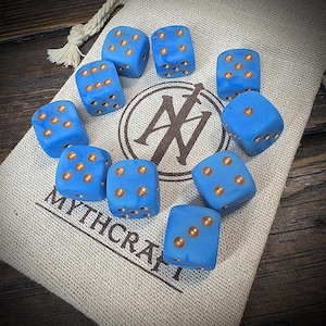 Könnte beinhalten: Ein Satz von zehn blauen Würfeln mit kupferfarbenen Augen, angeordnet auf einem beigen Stoffbeutel. Die Würfel sind leuchtend blau, die Augen kupferfarben. Auf dem Beutel steht "MYTHCRAFT" und ein Logo.